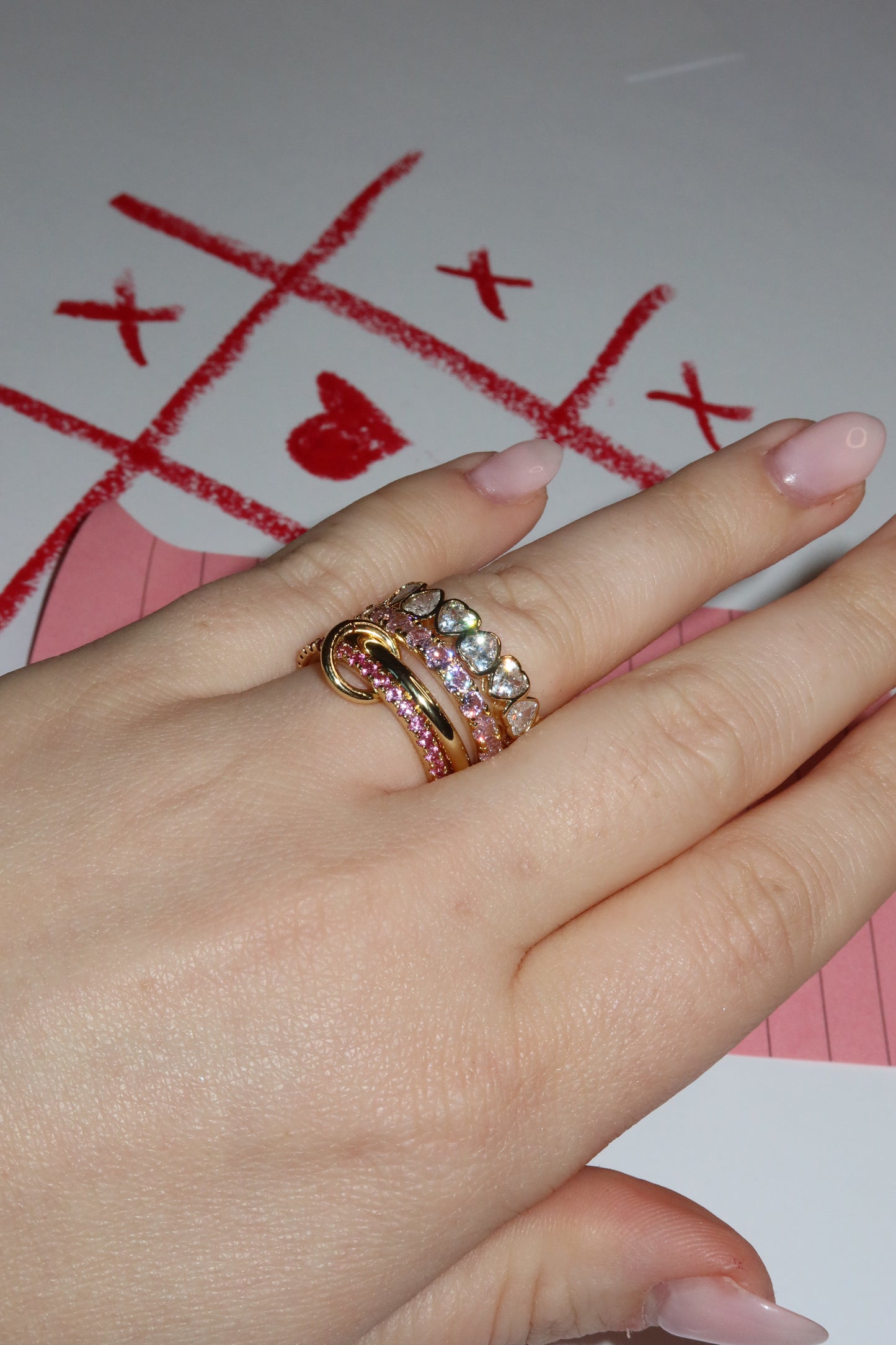 Hand wearing multiple rings with a red 'X' heart symbol on a white background