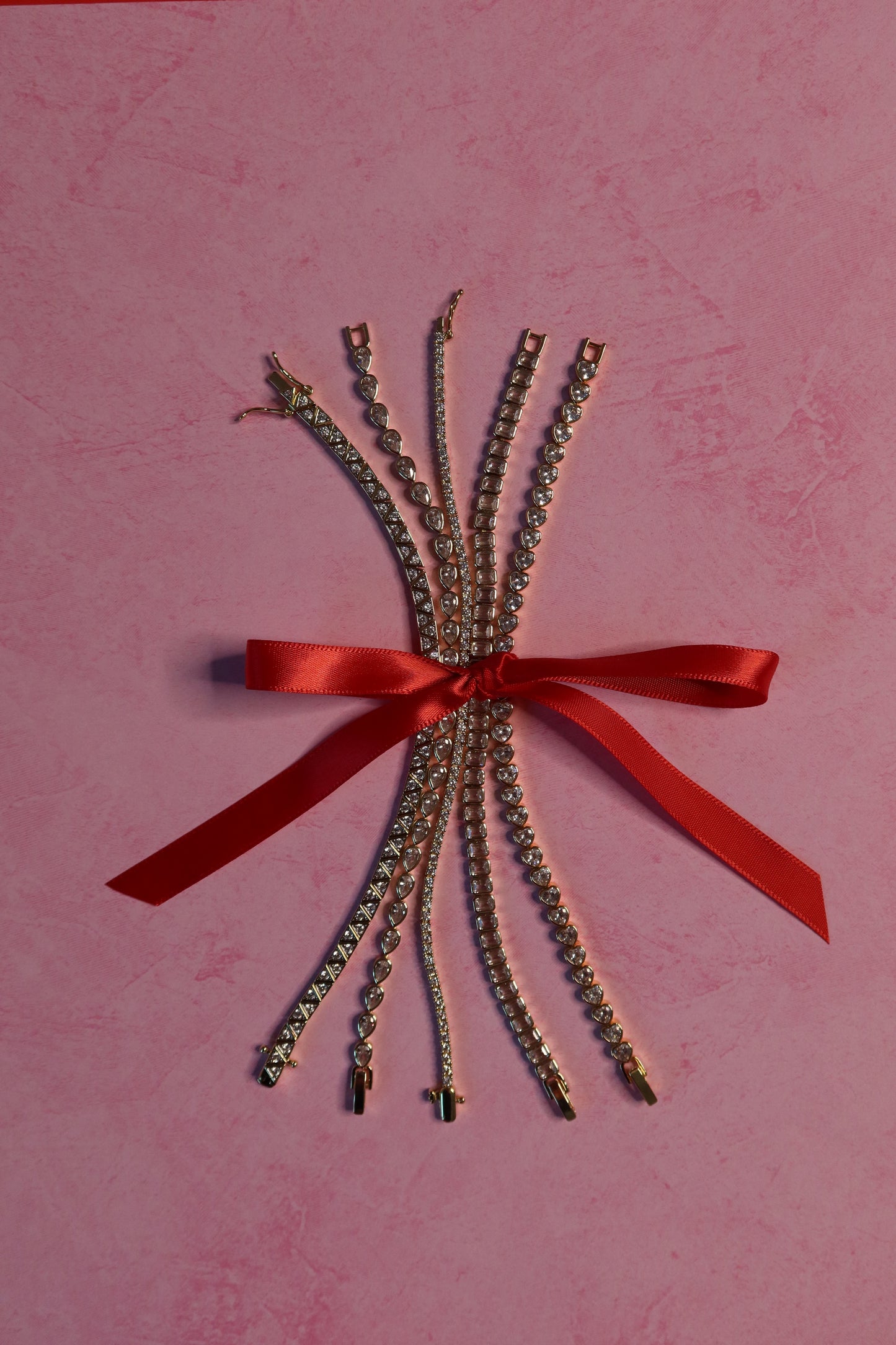 Bouquet of crystal bracelets with a red ribbon on a pink background