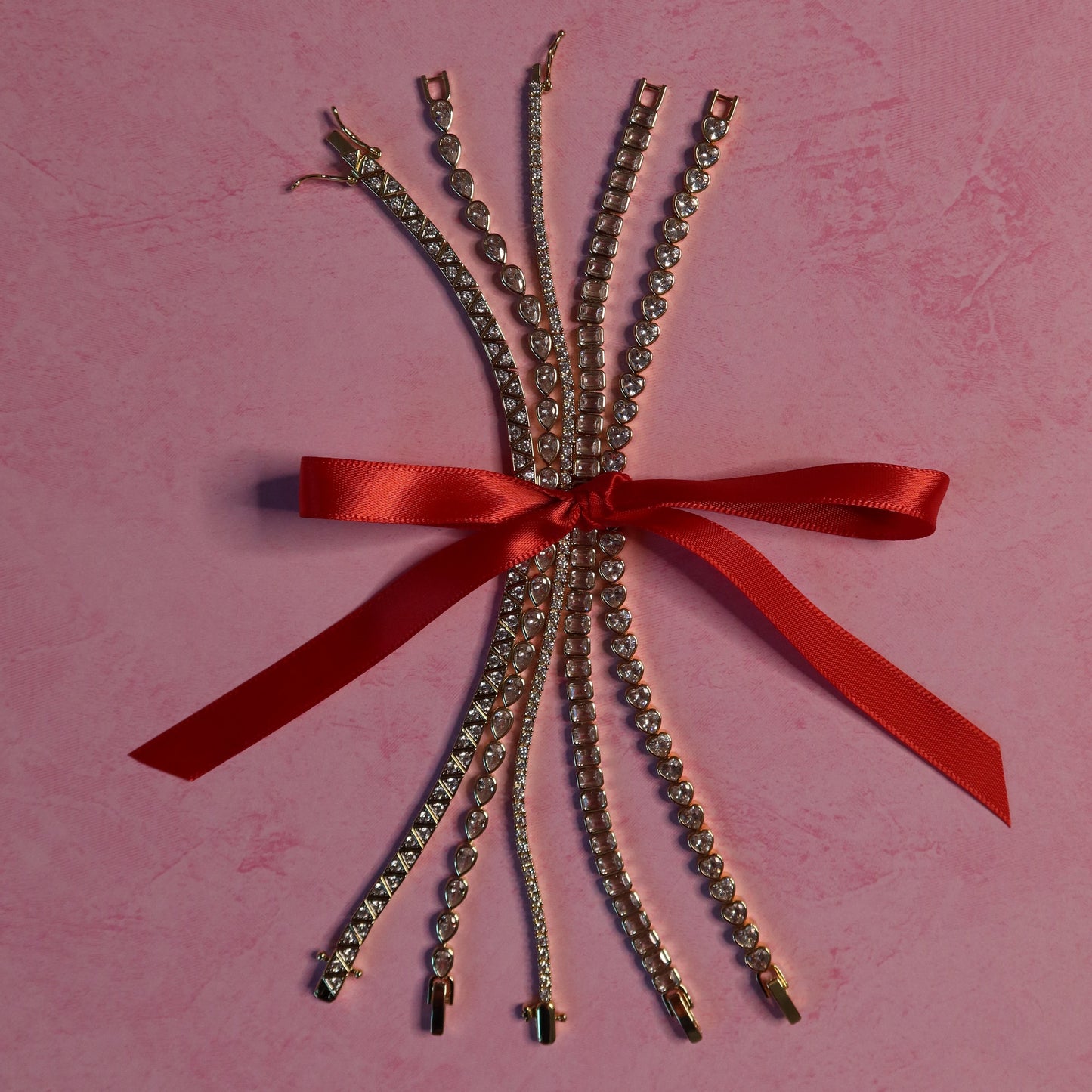 Bouquet of gold tennis bracelets with a red ribbon on a pink background